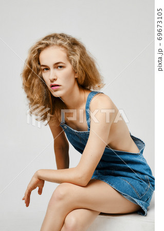 Pretty girl with blonde hair in jeans overalls posing over gray background Pretty girl with blonde hair in jeans overalls posing over gray background 69673105