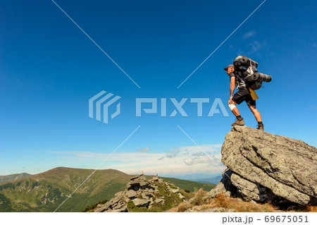 Young man with a backpack standing on top of a mountain and enjoying the view of the valley, the top of the Carpathians Eared stone. 69675051