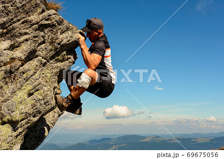 The man is engaged in mountaineering, climbs to the top, an epic view of the climber against the sky and mountains. 69675056