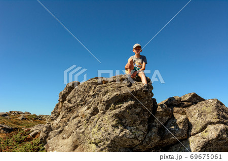 boy sitting on the edge of a large rocky rock, summer hike in the mountains, the top of the mountain. 69675061