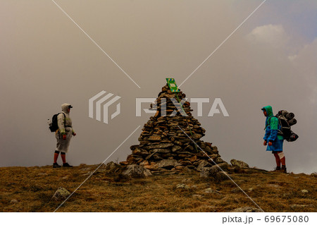Tourists in raincoats stand on top of the mountain, Mount Brebeneskul and fog, rain clouds on the Montenegrin ridge, happy tourists. 69675080