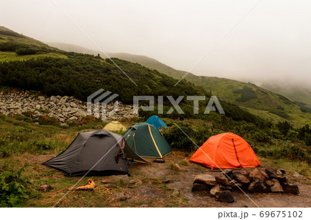 A small tent town in the mountains, tents by the lake in the mountains, the area near the lake Brebeneskul, the Carpathian mountains, fog and rain in the mountains. A small tent town in the mountains, tents by the lake in the mountains, the area near the lake Brebeneskul, the Carpathian mountains, fog and rain in the mountains. 69675102