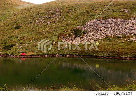 Tourists and tents near the lake, fog in the mountains near the lake, rain clouds in the Carpathians, a tent camp near the lake, Lake Brebeneskul. 69675104