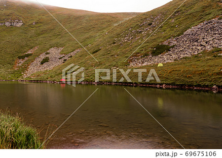 Tourists and tents near the lake, fog in the mountains near the lake, rain clouds in the Carpathians, a tent camp near the lake, Lake Brebeneskul. 69675106