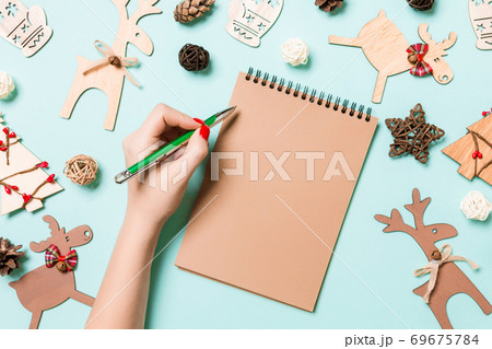 Top view of female hand making some notes in noteebok on blue background. New Year decorations and toys. Christmas time concept 69675784