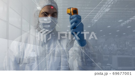 Healthcare worker wearing protective suit and using thermometer gun on himself with materials in bac 69677001