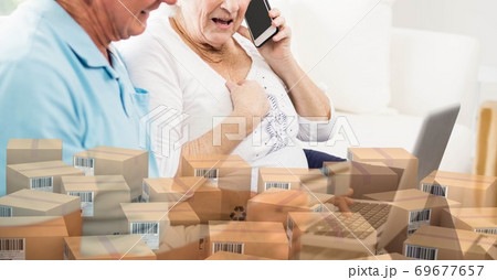 Caucasian senior couple using laptop shopping online with a pile of boxes 69677657