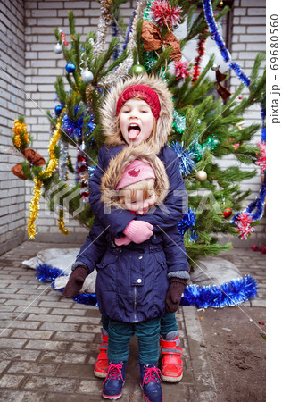 funny girls stand on street near Christmas tree. 69680560