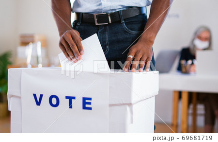 Unrecognizable african-american man putting his vote in the ballot box, usa elections and coronavirus. Unrecognizable african-american man putting his vote in the ballot box, usa elections and coronavirus. 69681719