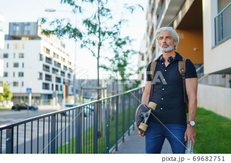 Portrait of mature man with skateboard outdoors in city, going back to work. 69682751