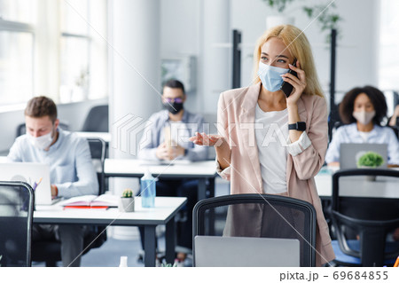 Young people back at work in office after lockdown. Business woman in protective mask speaks on phone with client Young people back at work in office after lockdown. Business woman in protective mask speaks on phone with client 69684855