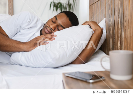 African Guy Sleeping Through Alarm-Clock Lying In Bed At Home African Guy Sleeping Through Alarm-Clock Lying In Bed At Home 69684857
