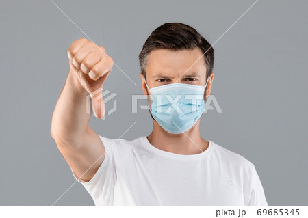 Man in protective mask showing thumb down on grey background 69685345
