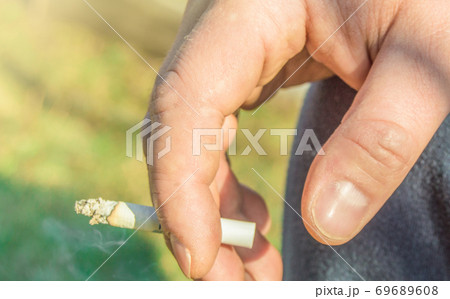 Close-up of an elderly man's hand Smoking a cigarette, outdoors, on a summer day Close-up of an elderly man's hand Smoking a cigarette, outdoors, on a summer day 69689608