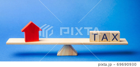 Wooden blocks with the word Tax and a house on scales. The concept of paying taxes on real estate and housing. Debt repayment. Mortgage, loan, credit. Apartment and apartments 69690930