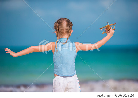 Happy little girl with toy airplane in hands on white sandy beach. Happy little girl with toy airplane in hands on white sandy beach. 69691524