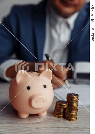 Businessman approves important contract. Piggy bank with stack of coins on desk close-up. Economy, business and management financial concept 69691867