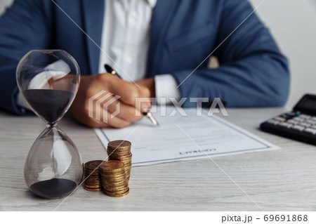 Businessman approves important contract in office. Stack of coins and hourglass on desk close-up. Time is money concept 69691868