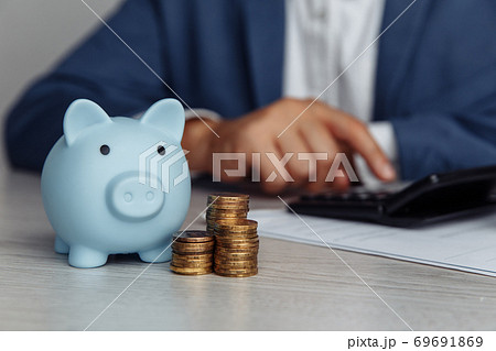 Man is counting profit on a calculator, blue piggy bank with stack of coins on wooden desk in office. Economy and management financial concept 69691869