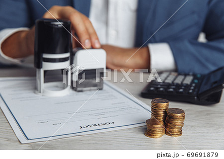 Businessman approves important contract. Stack of coins, contract and stamps on desk close-up. Business concept 69691879