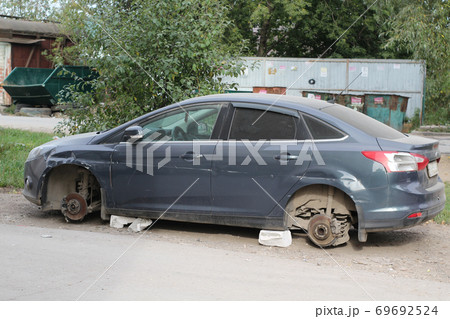 Old broken car after crash accident without wheels on bricks with trash cans 69692524