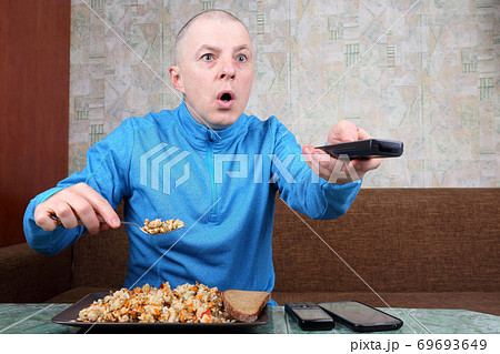 the man eats rice pilaf and stares of TV program the man eats rice pilaf and stares of TV program 69693649
