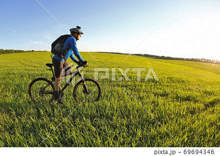 cyclist rides a bicycle on the green field towards the sun cyclist rides a bicycle on the green field towards the sun 69694346