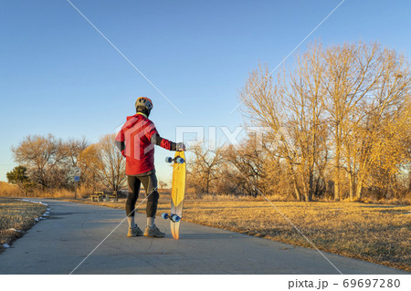 senior man with a cruising longboard on a bike trail senior man with a cruising longboard on a bike trail 69697280