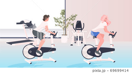 women working out on stationary bike fitness cardio training workout healthy lifestyle concept 69699414