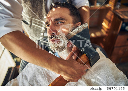 Handsome young man being shaved with an axe Handsome young man being shaved with an axe 69701146