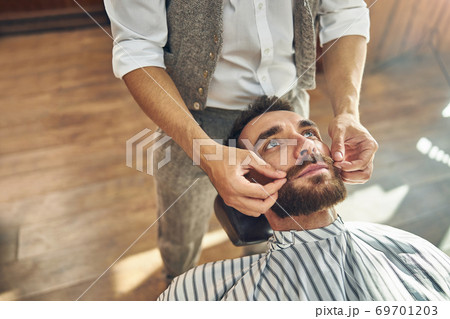 Skillful barber putting some hair wax on client moustache Skillful barber putting some hair wax on client moustache 69701203