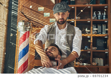 Serious barber shaving his client at a barbershop 69701234