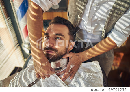 Brunette man receiving a clean shave from barber Brunette man receiving a clean shave from barber 69701235