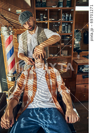 Professional hair-cutter turning head of his client ot the side to shave him 69701271