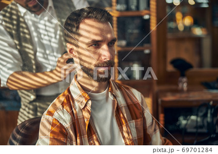 Serious barbershop client waiting for his barber to cut his hair 69701284