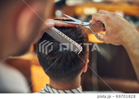 Skillful barbershop worker cutting hair of his visitor 69701828