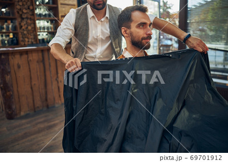 Qualified hair-groomer covering his visitor with a sheet Qualified hair-groomer covering his visitor with a sheet 69701912