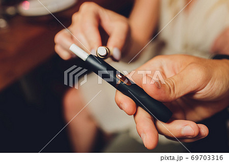 heat-not-burn tobacco product technology. Two woman e-cigarette in his hand before smoking. heat-not-burn tobacco product technology. Two woman e-cigarette in his hand before smoking. 69703316