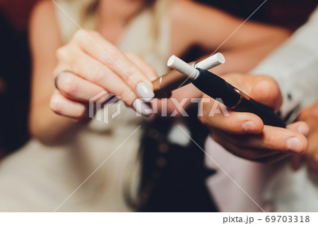 heat-not-burn tobacco product technology. Two woman e-cigarette in his hand before smoking. heat-not-burn tobacco product technology. Two woman e-cigarette in his hand before smoking. 69703318