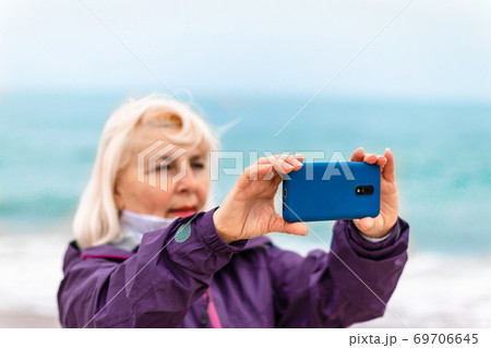 Woman traveler walking on vlychada beach and taking pictures by phone on the beach by the ocean, travel vacation concept Woman traveler walking on vlychada beach and taking pictures by phone on the beach by the ocean, travel vacation concept 69706645