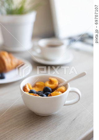 Delicious milk oatmeal with apricots and blueberries in a white bowl on a wooden table in the kitchen. Vertical photo 69707107