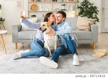 Young couple taking selfie with their dog in living room Young couple taking selfie with their dog in living room 69713810