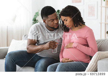Black pregnant woman feeling sick, husband giving glass of water Black pregnant woman feeling sick, husband giving glass of water 69713899