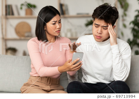 Asian Wife Showing Cheating Husband His Phone Suspecting Affair Indoors 69713994