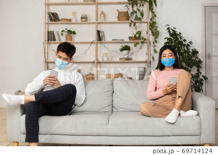 Asian Spouses In Medical Masks Texting Using Smartphones At Home 69714124
