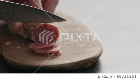 closeup man slicing cured sausage on a olive board with copy space 69721861