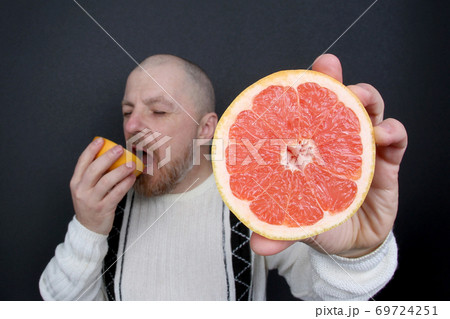 bearded man with a cut grapefruit in his hands bearded man with a cut grapefruit in his hands 69724251