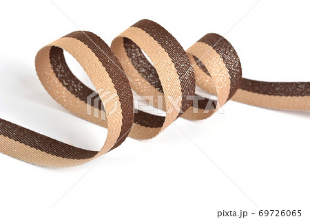 Brown beige Cotton ribbon, roll textilies on bobbin. strapping tape with curl on white backgroud. Brown beige Cotton ribbon, roll textilies on bobbin. strapping tape with curl on white backgroud. 69726065