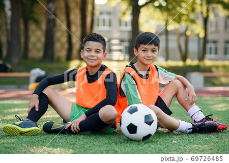 Good-looking joyful teen football players resting on the artificial grass covering of soccer field after training. Good-looking joyful teen football players resting on the artificial grass covering of soccer field after training. 69726485