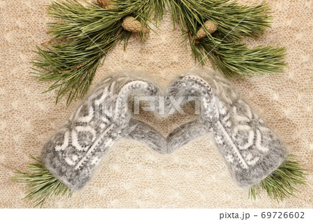 The heart of knitted down mittens with ornament with pine branches on top of the delicate white woollen canvas. The heart of knitted down mittens with ornament with pine branches on top of the delicate white woollen canvas. 69726602